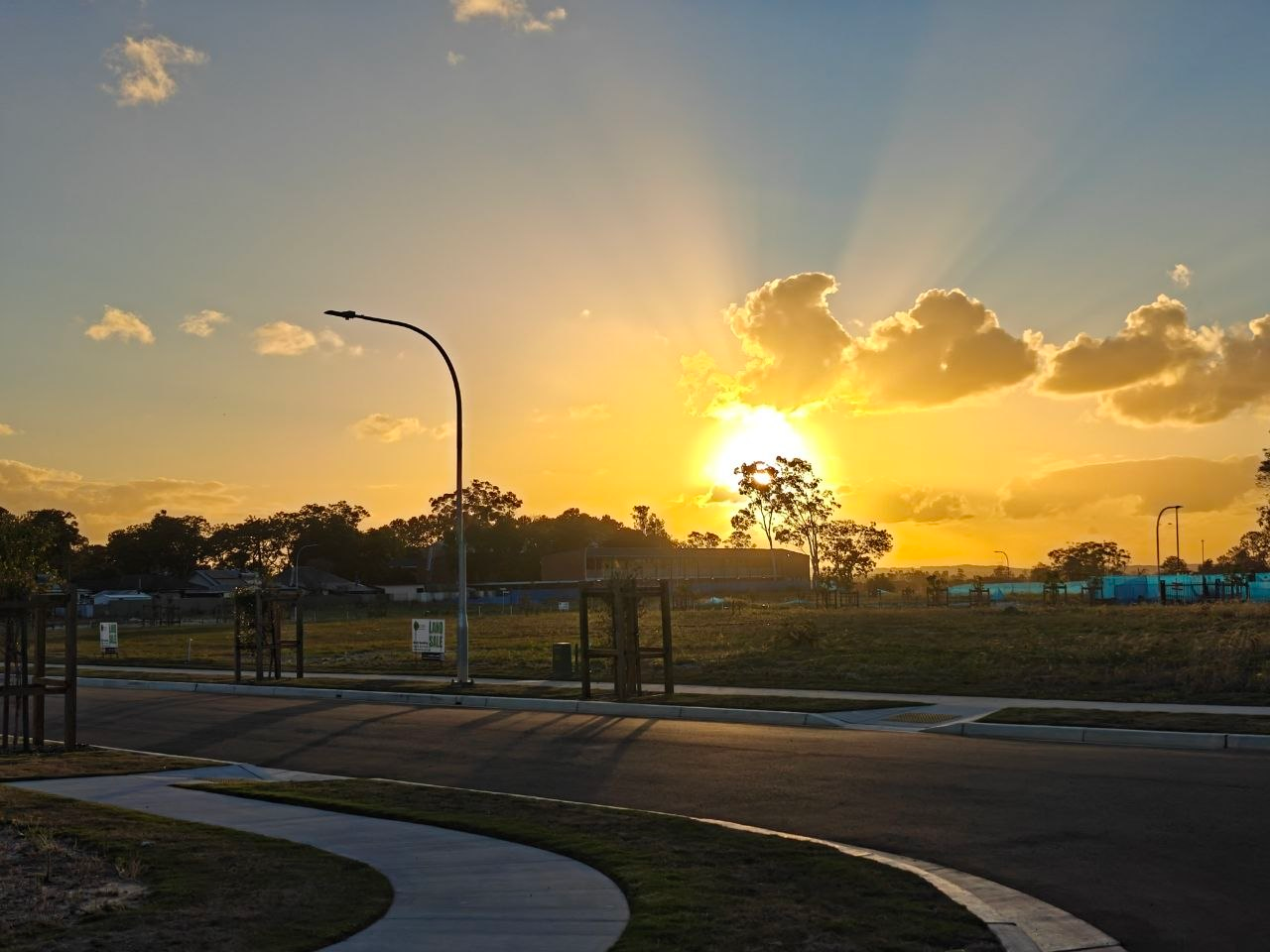 Golden evening sunlight through clouds above trees and a quiet street